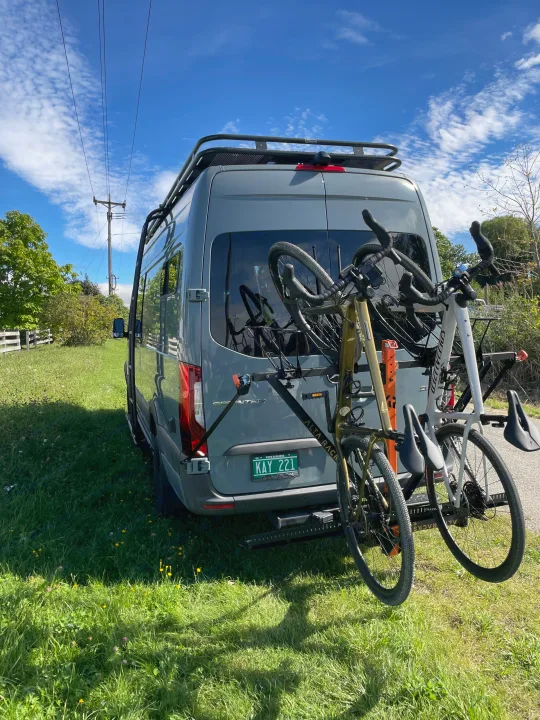 Grey RV rental van with two bicycles on its rear rack, parked on grass. Perfect for outdoor cycling adventures!. Mercedes-Benz Sprinter 2021