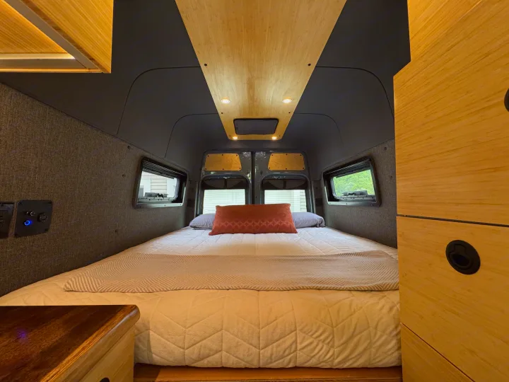 Relaxing RV rental interior showcasing a large bed, stylish wood ceiling & cabinetry, ambient lighting, and side windows.. Mercedes-Benz Sprinter 2021