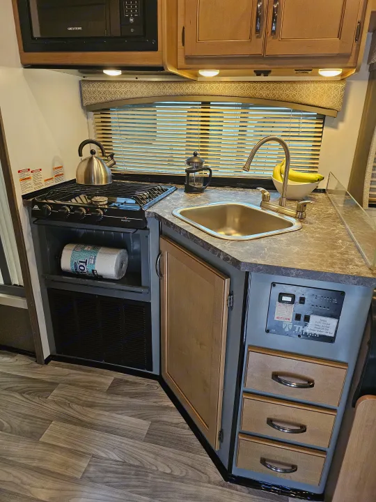 Clean & functional RV rental kitchen: Stove, sink, microwave, and ample storage for your road trip cooking needs.. Thor Four Winds 2021