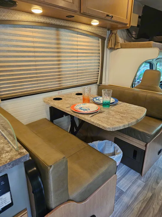 Cozy RV rental interior: dinette with set table, booth seating, and window blinds, perfect for meals on the go.. Thor Four Winds 2021