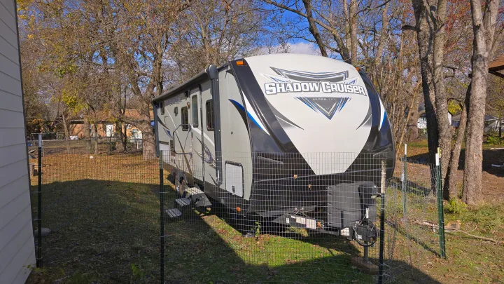 This grey and black Shadow Cruiser travel trailer, ideal for an RV rental, is parked in a grassy yard behind a wire fence.. Cruiser RV Shadow Cruiser 2019
