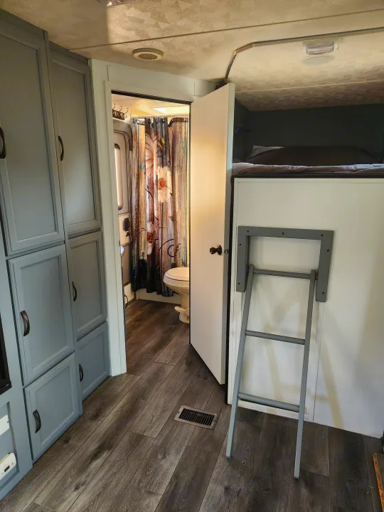 Inside an rv rental: gray cabinets, bathroom with floral curtain, and bunk bed with ladder. Compact living space.. Forest River Palomino Puma 2013