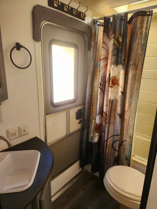 Compact RV rental bathroom features a sink, toilet, and patterned shower curtain. Bright door and storage hooks complete the space.. Forest River Palomino Puma 2013