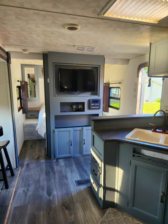 Interior of a modern rv rental, showcasing a gray-themed living area with kitchen, built-in TV, dark wood-look floor, and rear bedroom.. Forest River Palomino Puma 2013