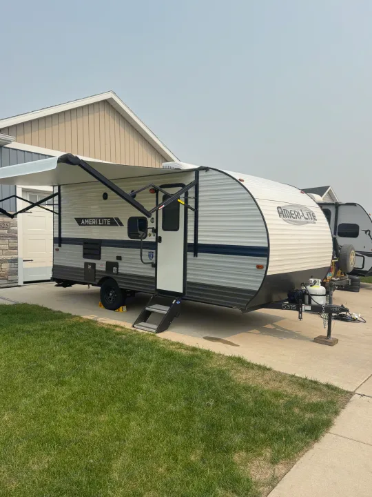 An Ameri-Lite RV rental, with its awning extended, parked on a residential driveway, ready for adventure.. Gulf Stream Ameri-Lite Super Lite 2022