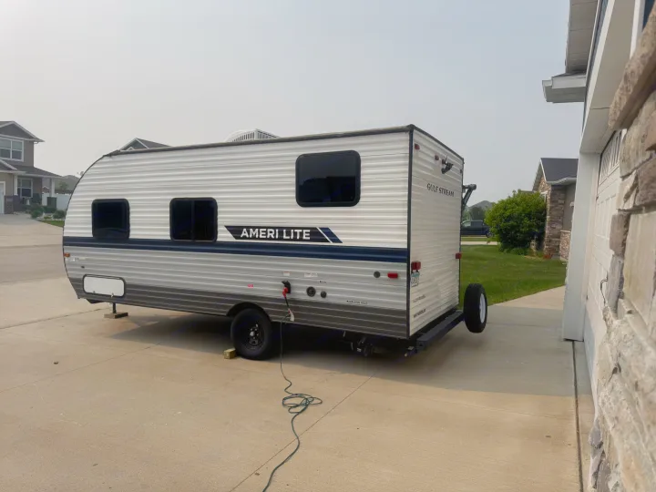 A silver Gulf Stream Ameri Lite travel trailer RV sits parked on a concrete driveway, plugged in. Ideal for an RV rental.. Gulf Stream Ameri-Lite Super Lite 2022