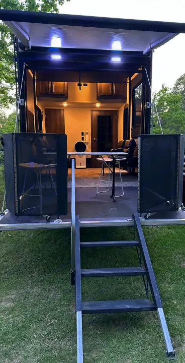 This RV rental features an open ramp converted into an illuminated patio, with seating, side barriers, and stairs to the ground.. Keystone RV Carbon Toy Hauler 2018