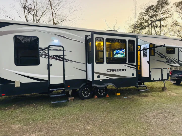 Impressive Carbon RV rental, a fifth wheel, set up on grass with extended slide-outs and interior lights on.. Keystone RV Carbon Toy Hauler 2018