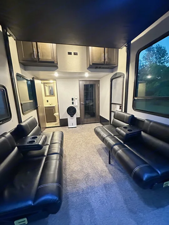 This RV rental interior features facing black sofas, a bathroom, and a central fan, offering a comfortable space.. Keystone RV Carbon Toy Hauler 2018