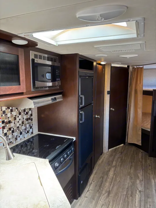 Step inside this rv rental! Features a well-equipped kitchen with microwave, stove, fridge, a bathroom door, and bunk beds.. Forest River Cherokee 2017