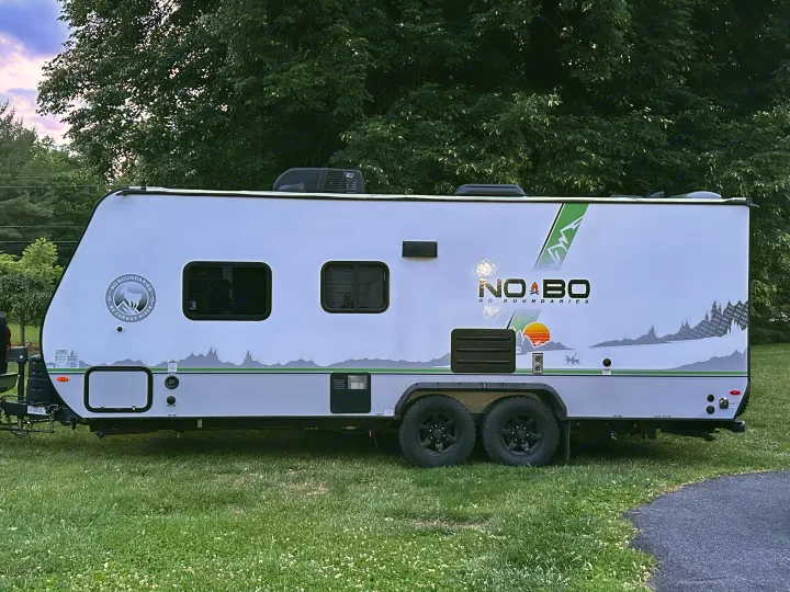 This white No Boundaries travel trailer, an ideal RV rental, is parked on grass for outdoor adventures.. No Boundaries 19 2021