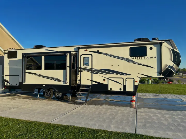 A cream Montana High Country fifth-wheel RV parked on a concrete drive. Perfect for an rv rental outdoor adventure.. Keystone RV Montana High Country 2021