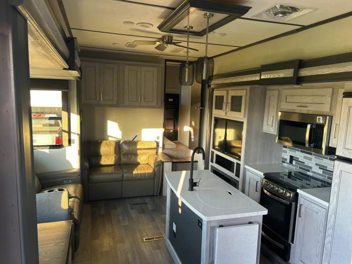 Spacious RV rental interior with a modern kitchen island, stainless steel appliances, and a comfortable leather sofa in the living area.. Keystone RV Montana High Country 2021