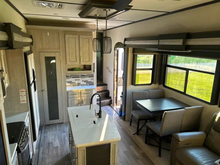 Spacious RV rental interior with a modern kitchen island, dining area, and comfortable living space under natural light.. Keystone RV Montana High Country 2021