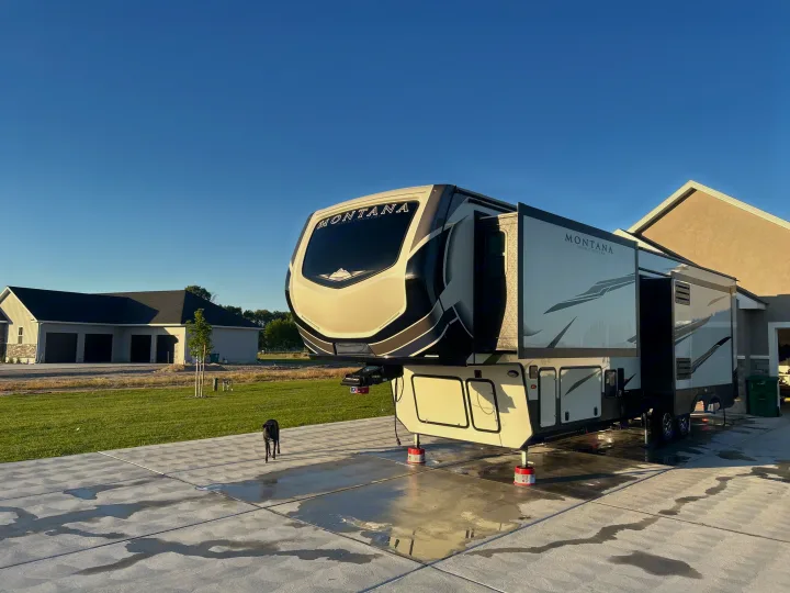 Large Montana fifth-wheel RV rental set up on a sunny driveway with extended slide-outs and a black dog.. Keystone RV Montana High Country 2021