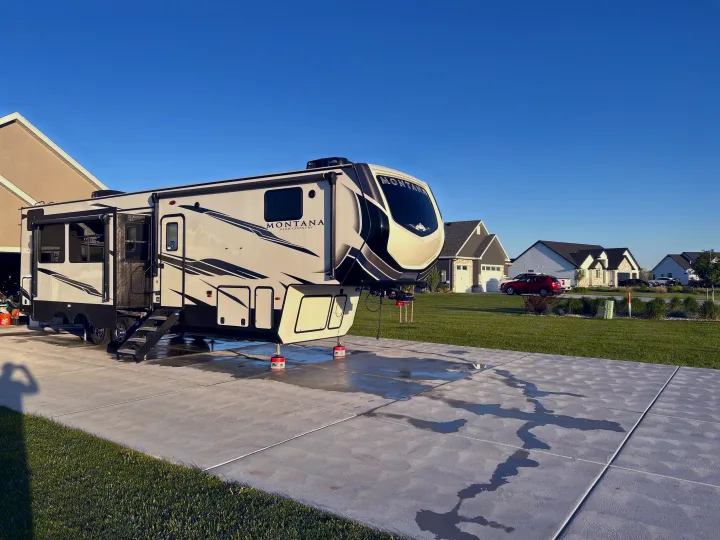Montana fifth-wheel RV rental, parked on a sunny driveway with fresh water streaks after a wash.. Keystone RV Montana High Country 2021