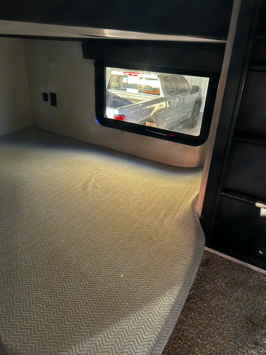 RV rental bunk: cozy interior bed with power outlets, window view of a parked truck outside.. Keystone RV Montana High Country 2021