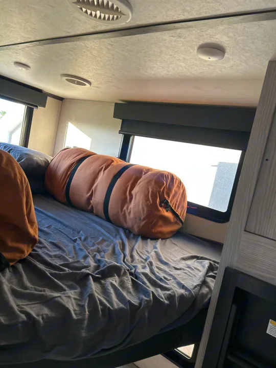 Comfortable RV rental bunk bed with pillows, gray sheets, and bright windows, showing a cozy interior space.. Keystone RV Montana High Country 2021