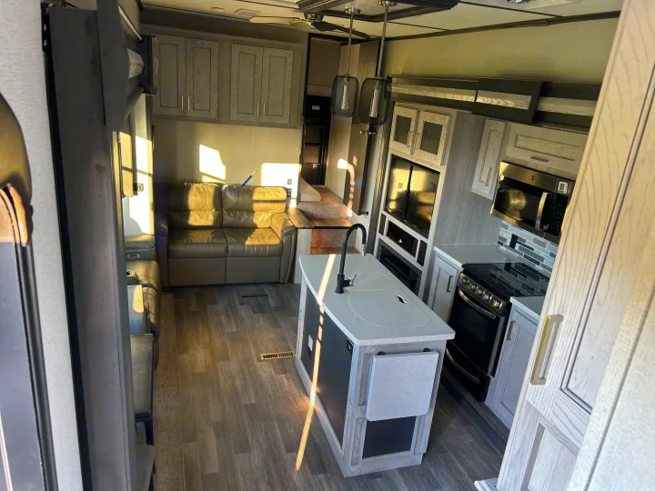 Inside a modern RV rental: a bright kitchen island, living area with sofa, and stairs to a raised bed.. Keystone RV Montana High Country 2021
