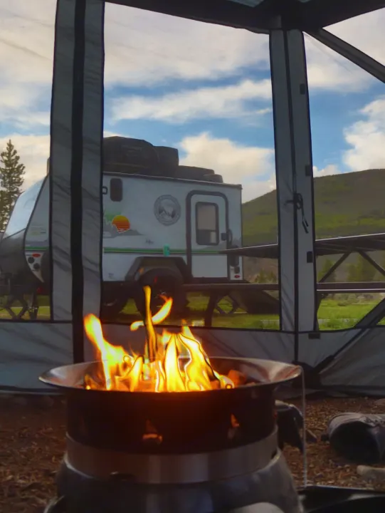 Campfire from a screened tent, viewing an RV rental trailer parked in a scenic mountain setting.. No Boundaries 10 Toy Hauler 2022