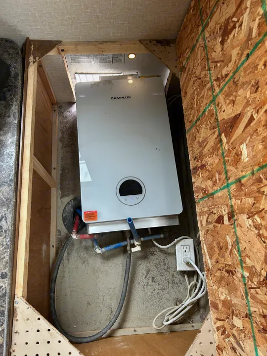 View inside an RV rental utility area: Camplux tankless water heater, water lines (red/blue), and power outlet.. Crossroads Z-1 2017