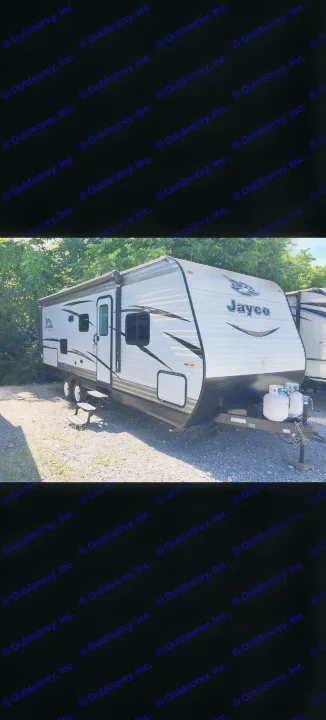 White Jayco travel trailer with awning and propane tanks, parked on gravel. Perfect for RV rental adventures.. Jayco Jay Flight 2018