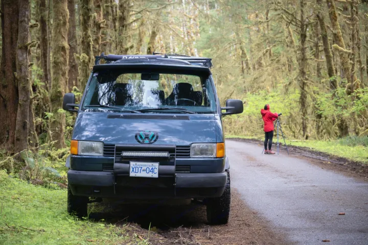 Exploring BC's mossy forests with an RV rental van. A person sets up a tripod on the road for nature photography.. Volkswagen eurovan 1996