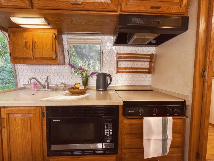 This RV rental kitchen features wood cabinets, white hexagonal tile backsplash, a sink, microwave, and stovetop.. Airstream Classic 2002