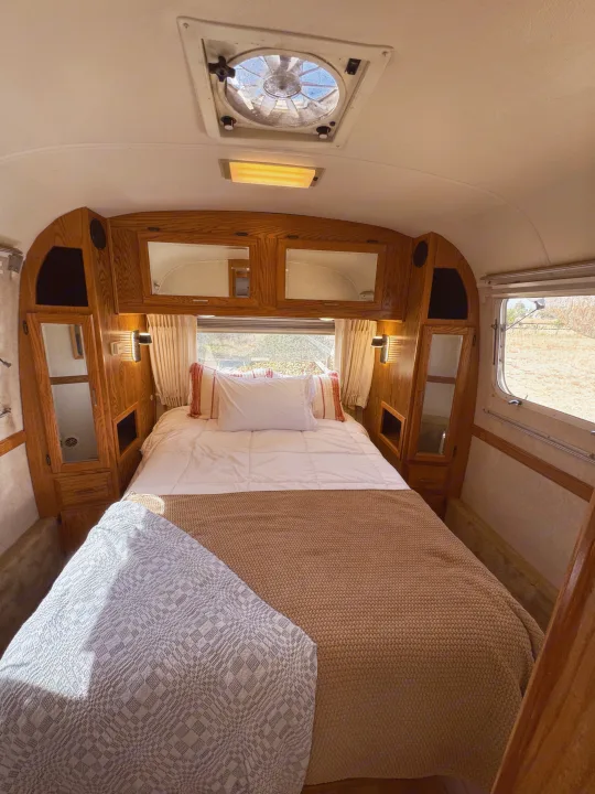 Comfortable RV rental bedroom with a neatly made bed, classic wooden interior, and an overhead fan for ventilation.. Airstream Classic 2002