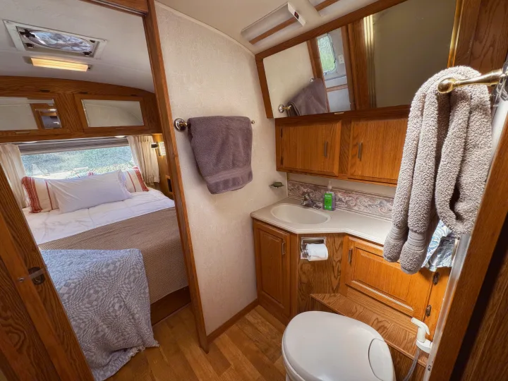 RV rental interior featuring a cozy bedroom with a large window and a compact bathroom with sink, toilet, & wood cabinetry.. Airstream Classic 2002