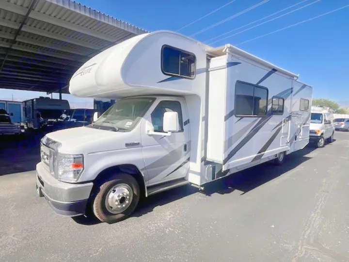 This white Class C RV for rental, featuring an extended awning and sleek graphics, is parked outdoors.. Thor Freedom Elite 2022