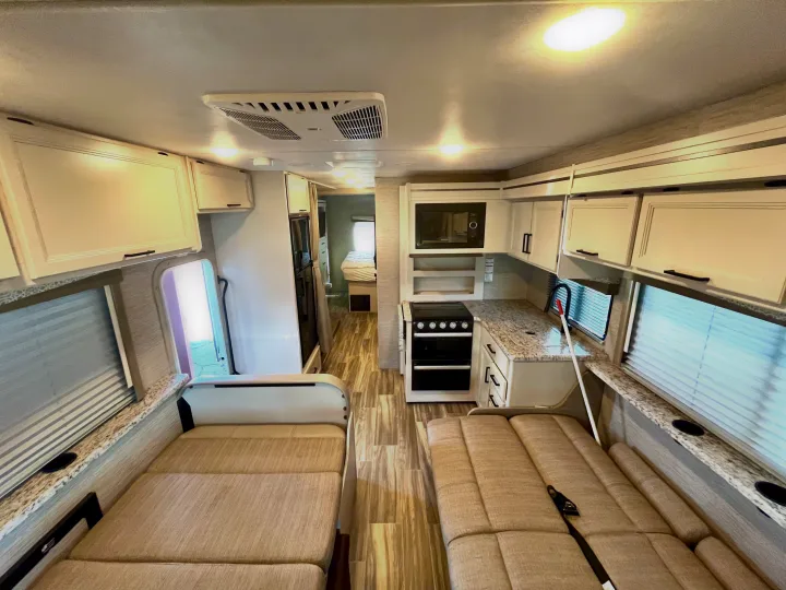 Bright, modern RV rental interior featuring a full kitchen, comfortable dinette, and visible sleeping area. Ideal for travel!. Thor Freedom Elite 2022