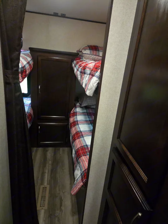 View of an **RV rental** bedroom with cozy plaid bunk beds, dark wood cabinetry, and a floor vent visible.. Jayco Jay Flight SLX 2018