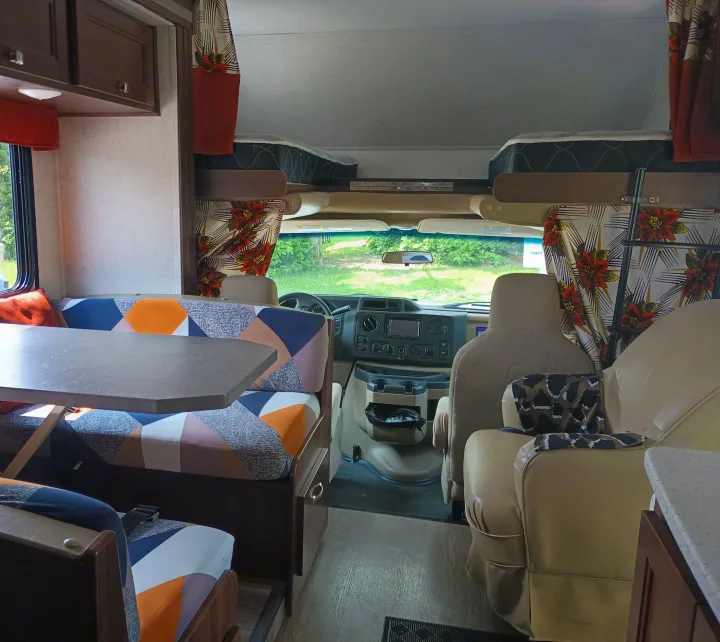 Vibrant RV rental interior: Dinette with geometric cushions, overhead bunks, cockpit view. Ready for comfortable travel.. Forest River Sunseeker 2018