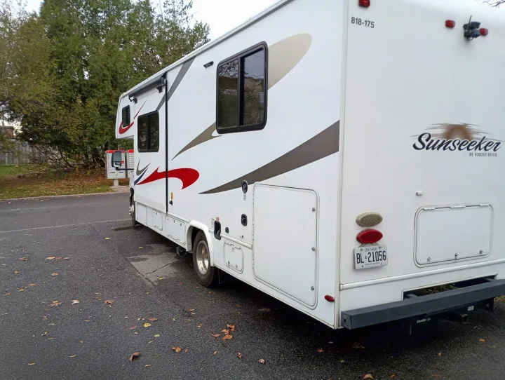 White Sunseeker rv rental, featuring bold graphics, windows, and an Ontario license plate (BL 21056), parked on asphalt.. Forest River Sunseeker 2018