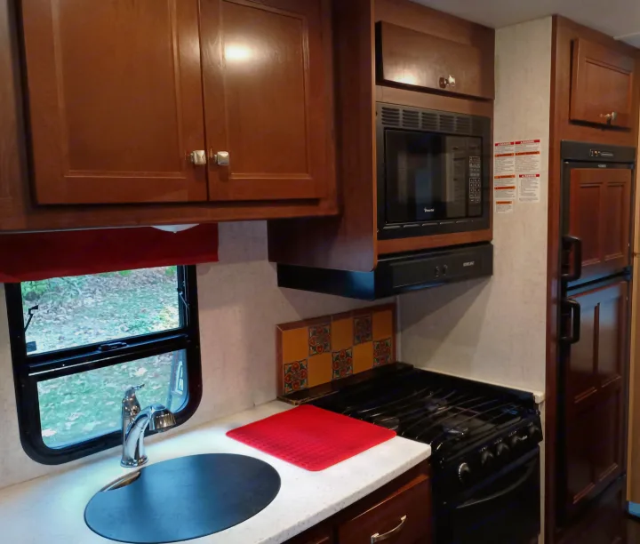 Bright RV rental kitchen with ample counter space, wood cabinets, and modern appliances including a microwave, stove, and sink.. Forest River Sunseeker 2018