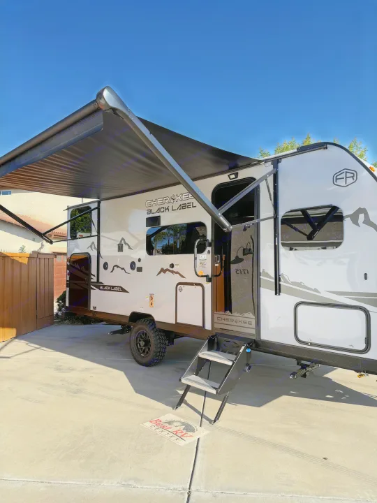 Cherokee Black Label RV with extended awning, ideal for RV rental. Parked on a driveway, ready for travel & camping.. Cherokee WOLF PUP BLACK LABEL 17JWBL 2025