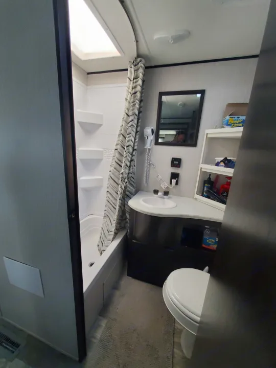 Inside an rv rental: a compact bathroom with shower, sink, toilet, and mirrored vanity.. Heartland RVs Prowler 2021