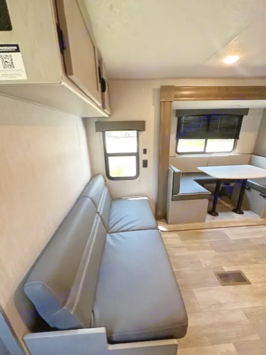 RV rental interior: A cozy living space with a large grey sofa and dinette seating, featuring wood-look floors and windows.. Forest River Forest River Viking 2025