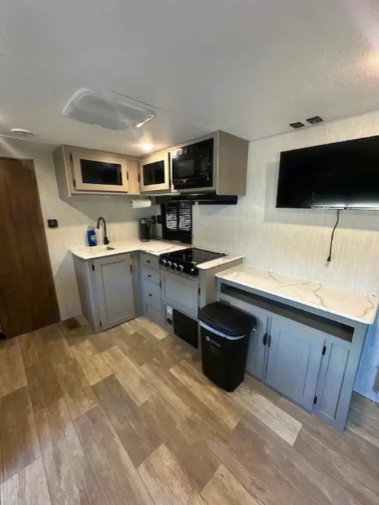 This modern RV rental features a compact kitchen with a microwave, stove, sink, ample storage, and a TV, all on wood-look floors.. Forest River Forest River Viking 2025