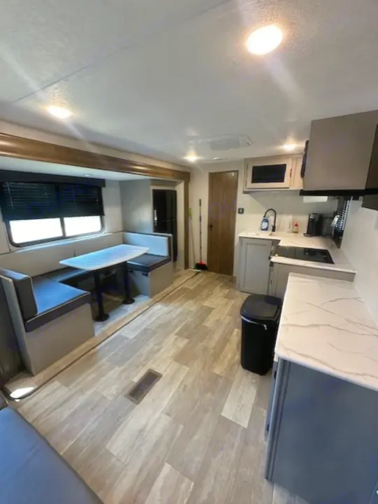 Modern RV rental interior: L-shaped dinette on left, kitchen with light grey cabinets/white counters on right. Wood-look flooring.. Forest River Forest River Viking 2025