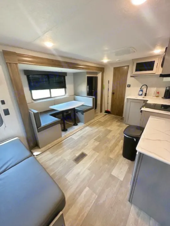 This clean RV rental interior features a kitchen, dining booth, and a sofa/bed area on wood-look floors, offering a comfortable travel space.. Forest River Forest River Viking 2025