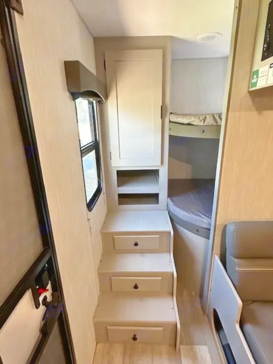 Light-colored RV rental interior featuring storage steps, a cabinet, window, and bunk beds. Perfect for camper trips.. Forest River Forest River Viking 2025