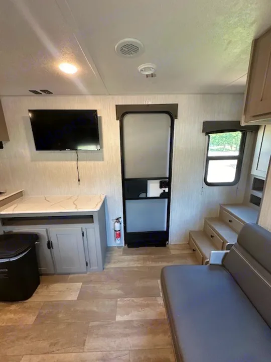 Bright RV rental interior features a kitchen counter, TV, sofa, and steps to a sleeping area, ideal for travel.. Forest River Forest River Viking 2025