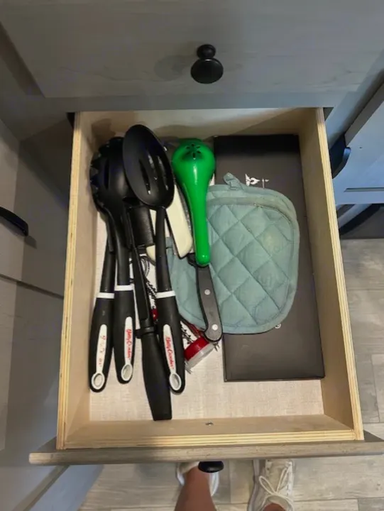 Inside an rv rental, an open kitchen drawer reveals cooking utensils, including a large green one, and a quilted pot holder.. Forest River Forest River Viking 2025