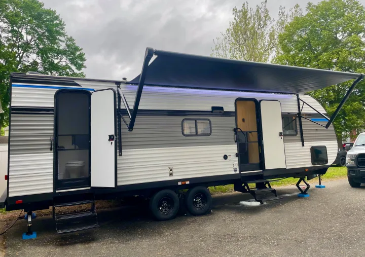 Experience comfort on wheels with this RV rental! A grey & white travel trailer, set up with an extended awning & stabilizing jacks.. Heartland RVs Pioneer Trail Blazer 2024