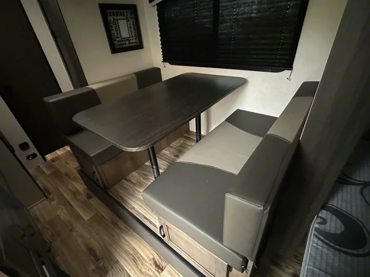 Cozy RV rental dinette featuring booth seating, a dark table, and window blinds. Perfect for road trips.. Venture RV SL169VUD 2023