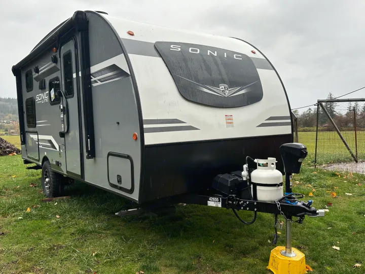 Rain-kissed grey Sonic Lite travel trailer, an ideal RV rental ready for adventure, parked on grass.. Venture RV SL169VUD 2023