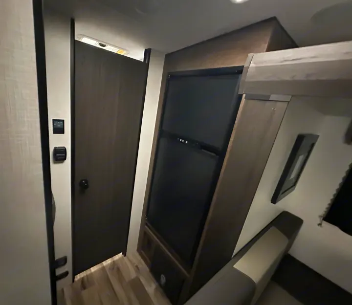Interior view of an RV rental, showcasing a compact living space with a refrigerator, door, and dinette.. Venture RV SL169VUD 2023