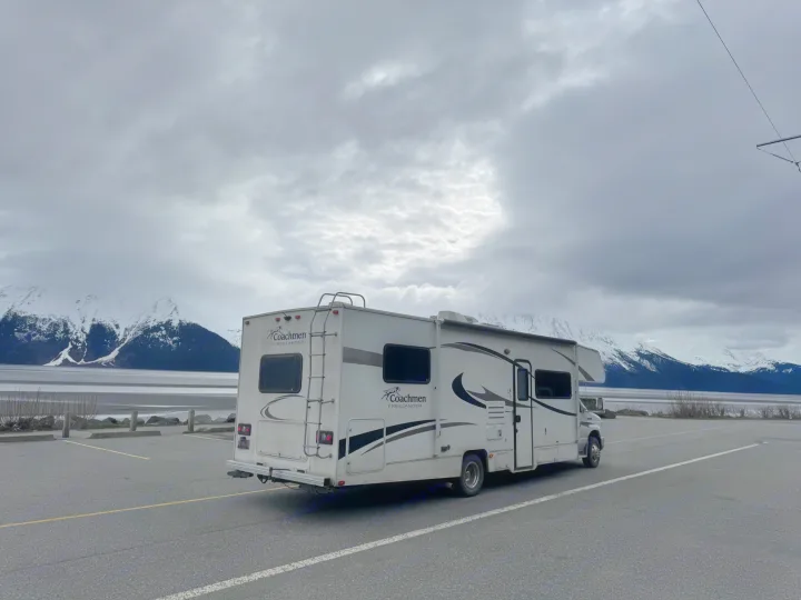 Coachmen RV rental parked by snowy mountains and a calm body of water under a cloudy sky. Perfect for scenic road trips.. Coachmen Freelander 2014